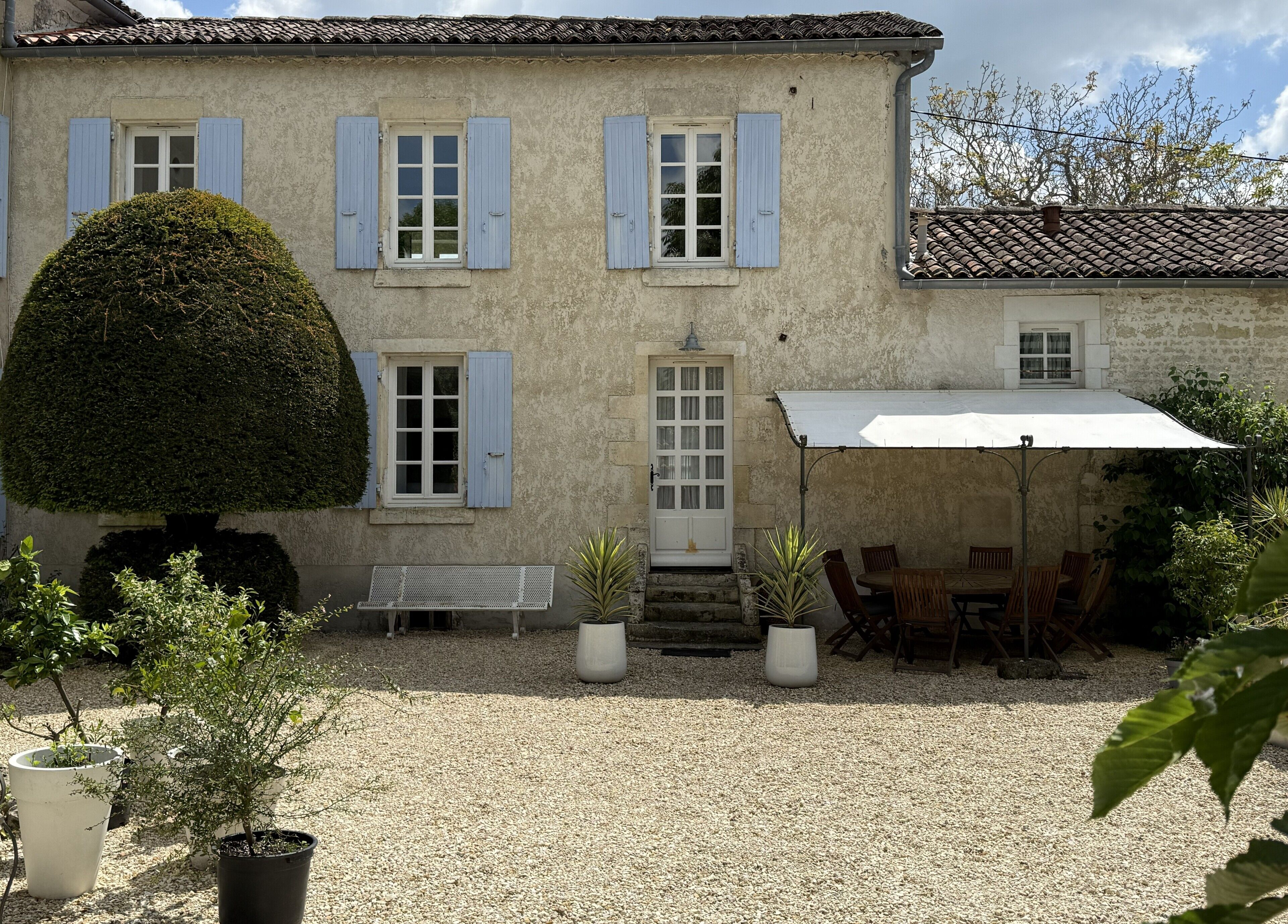 A two-story building with a gravel courtyard, a covered patio with chairs, and potted plants.