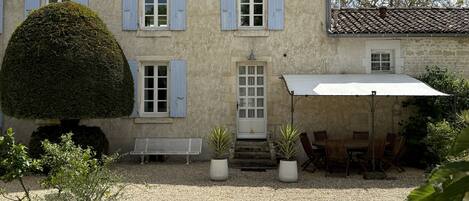 A two-story building with a gravel courtyard, a covered patio with chairs, and potted plants.