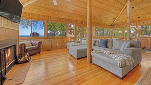 Eine geräumige Holzhütte mit Kamin, zwei Sofas und einem Deckenventilator.