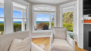 A room with large windows offering a view of the ocean, a fireplace, and two armchairs. - Lakefront | South Beach | 6BR (South Haven)