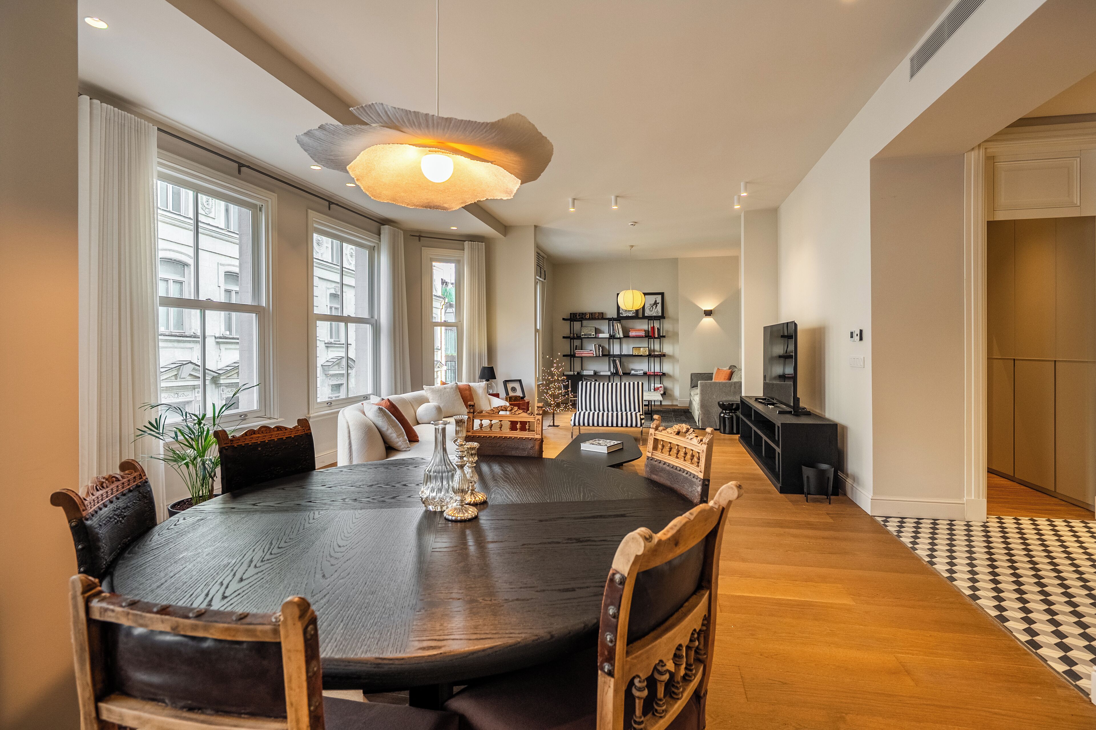 A spacious living room with a large round table, comfortable seating, a fireplace, and a bookshelf.