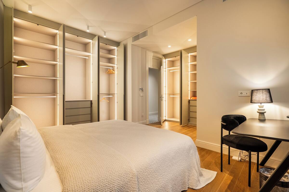 A modern bedroom with a large bed, built-in shelving, a desk, and a chair.