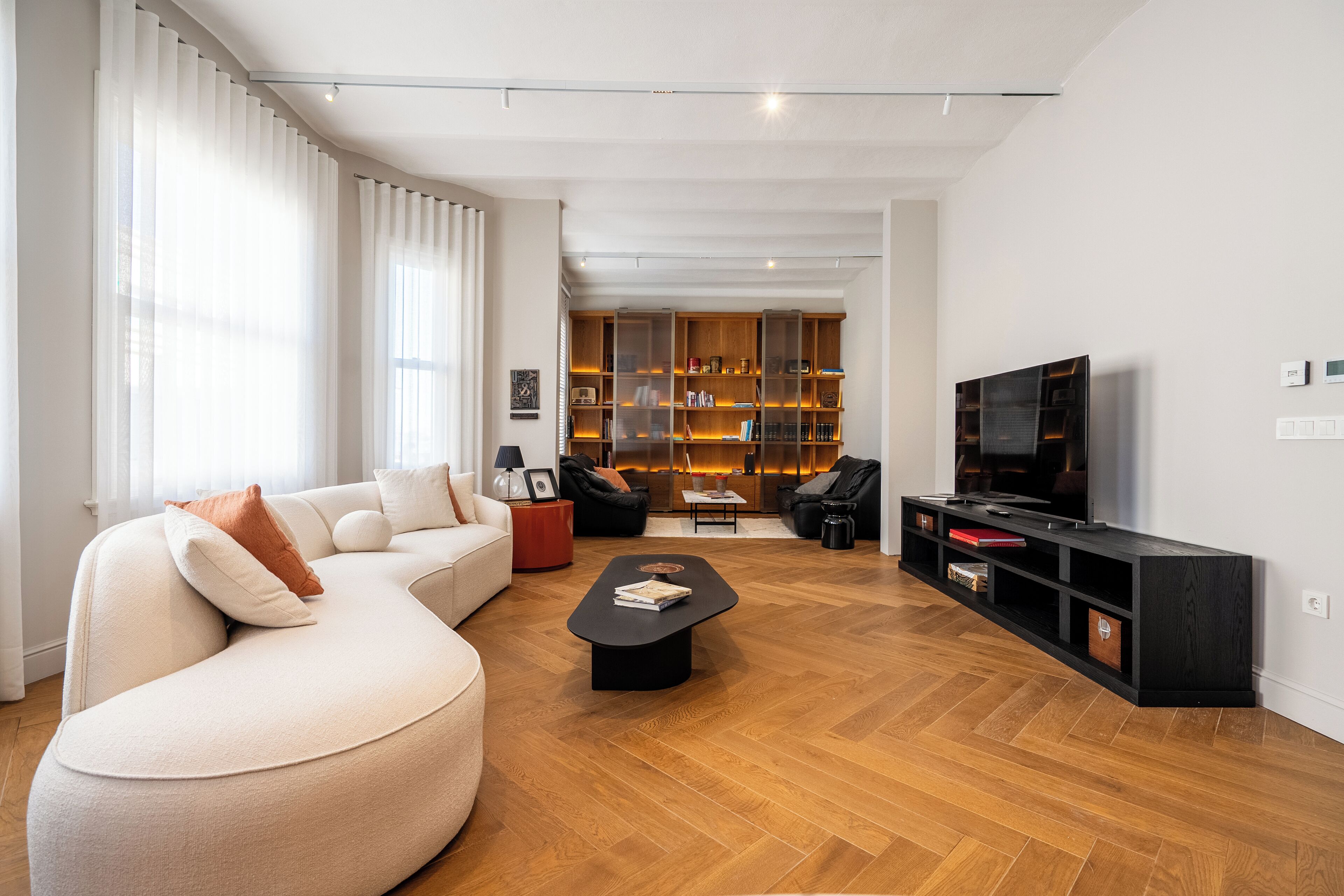Una sala de estar moderna con un sofá seccional, una mesa de centro, un mueble para televisión y una estantería.