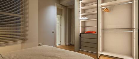 Une chambre à coucher avec un lit, un dressing avec des étagères et une fenêtre avec des stores.
