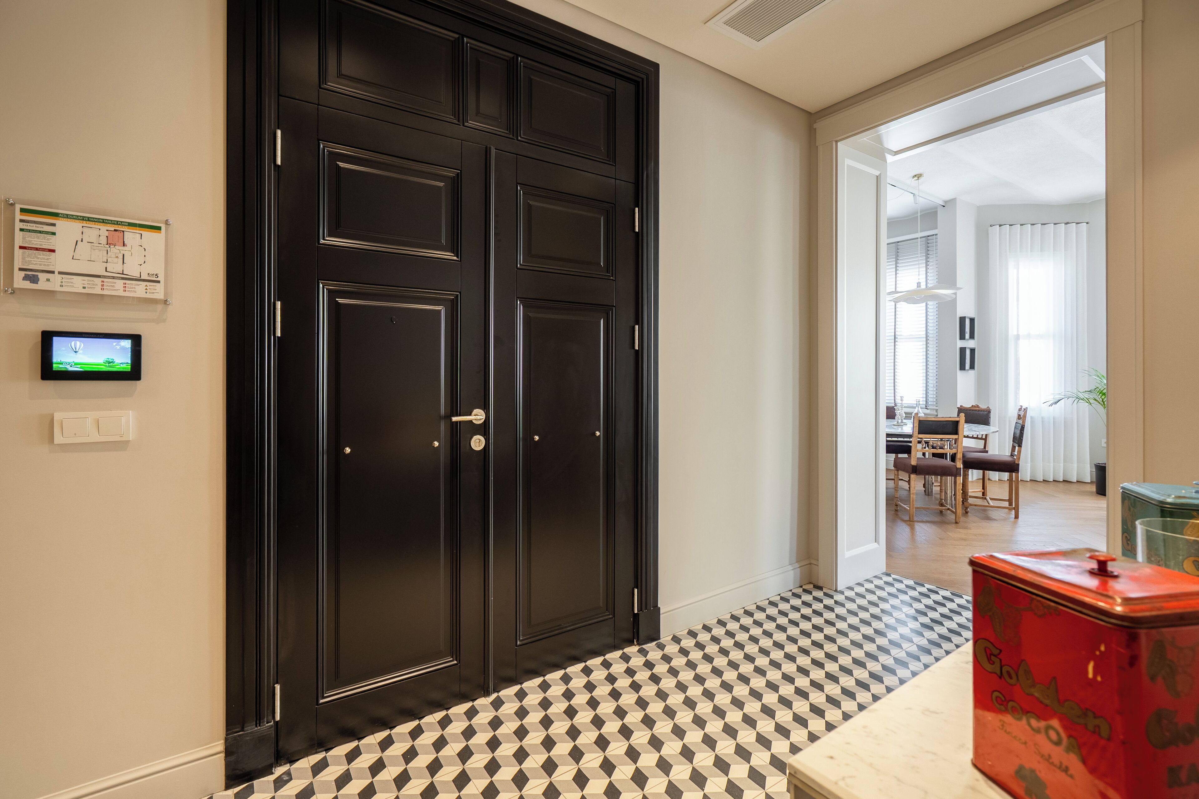 A hallway with a black double door, a black and white checkered floor, a red tin labeled 'Cocoa', and a dining area visible through an open door.