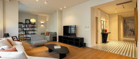 Una sala de estar moderna con un sofá, una mesa de centro negra, un sillón a rayas, un televisor sobre un mueble negro y una estantería.