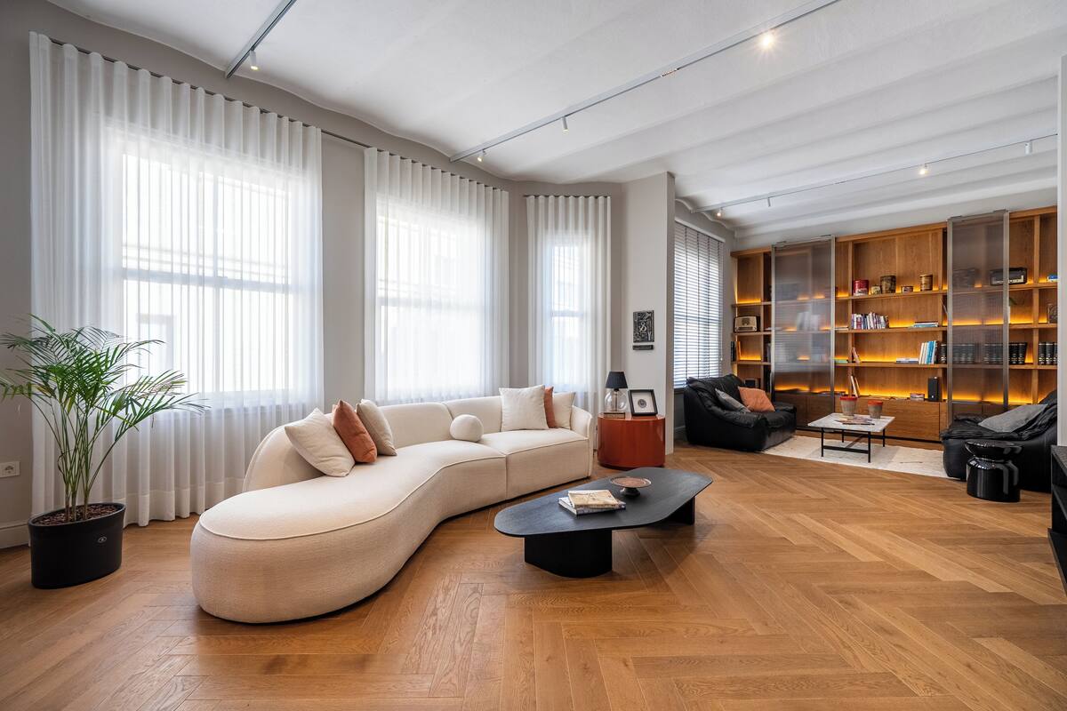 A modern living room with a curved sofa, a coffee table, and a bookshelf.