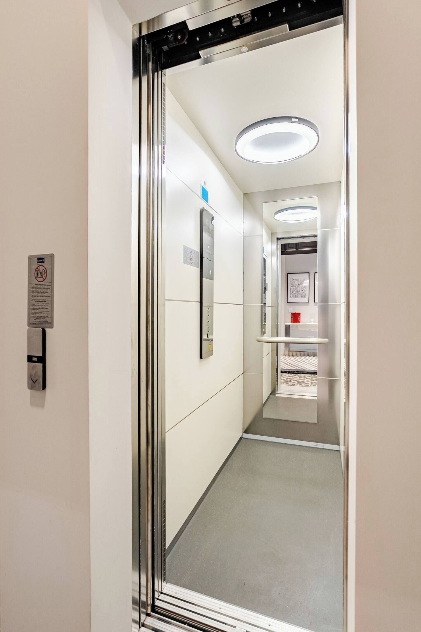A narrow, well-lit hallway with a mirrored wall, a handrail, and a door at the end.