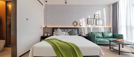 Una habitación de hotel moderna con una cama grande, un sofá verde, una mesa de centro redonda y una pared con diseño.