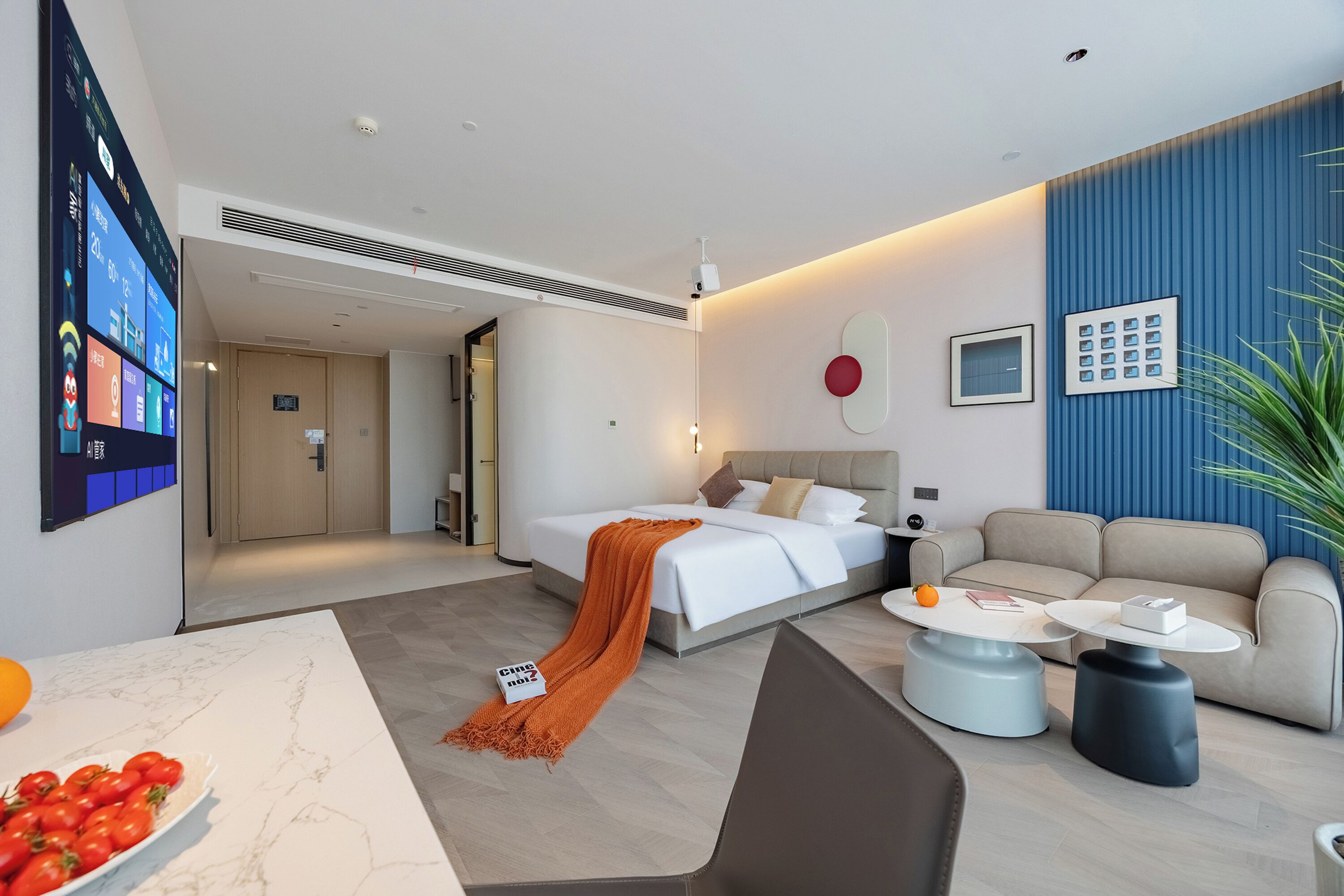 A modern hotel room with a bed, a sofa, a coffee table, and a TV displaying room information.