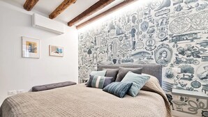 Een slaapkamer met een groot bed, een hoofdeinde en een muur vol oude illustraties.
