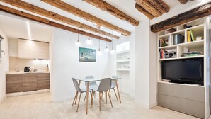 Een moderne keuken met houten balken, een eethoek met een glazen tafel, en een televisie op een plank.