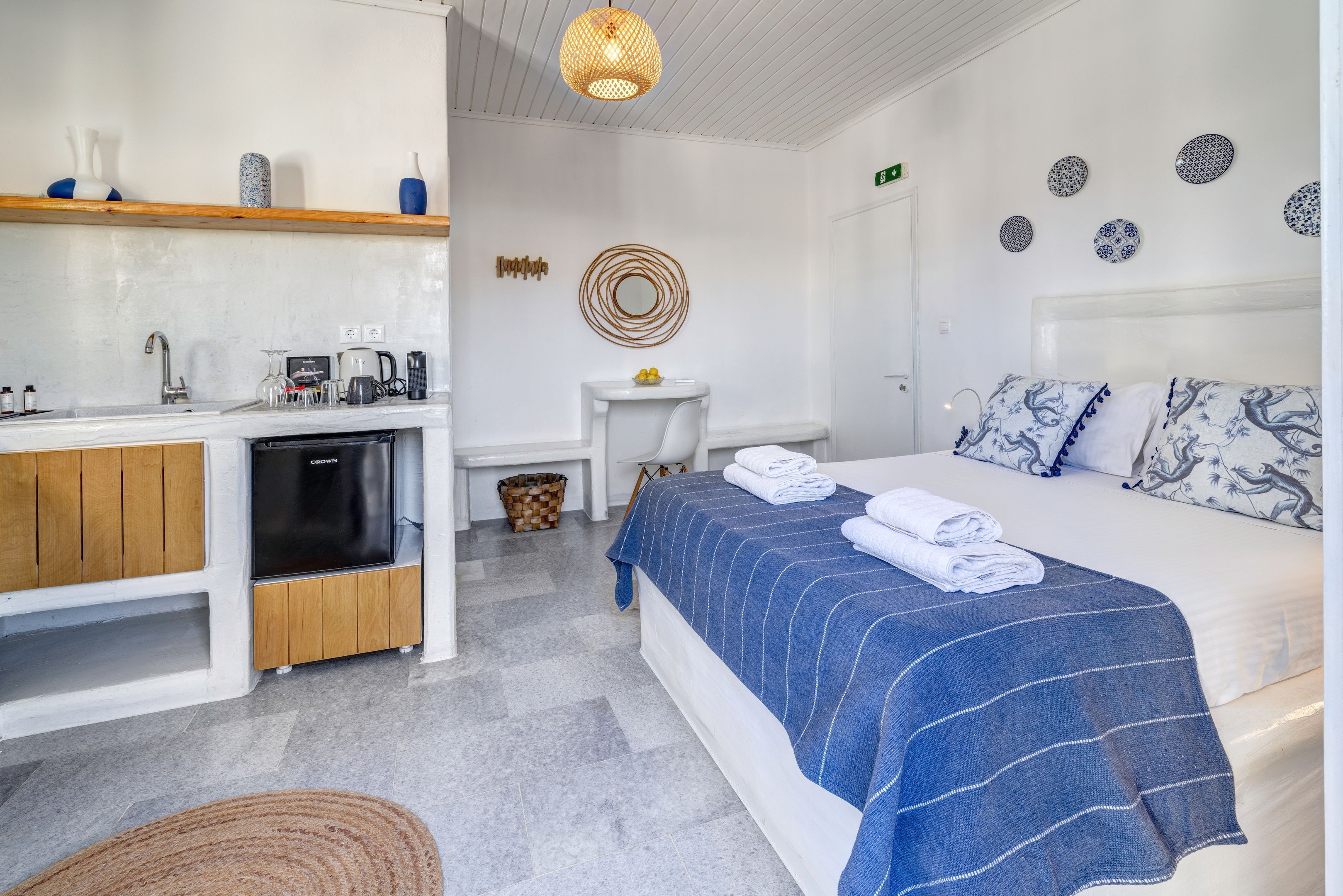 A modern hotel room with a bed, a small kitchenette, a bathroom, and a dining area.