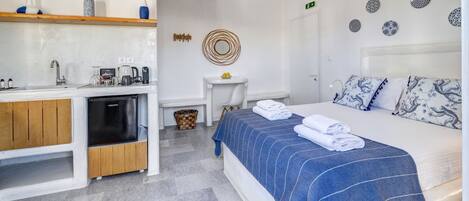 A modern hotel room with a bed, a small kitchenette, a bathroom, and a dining area.