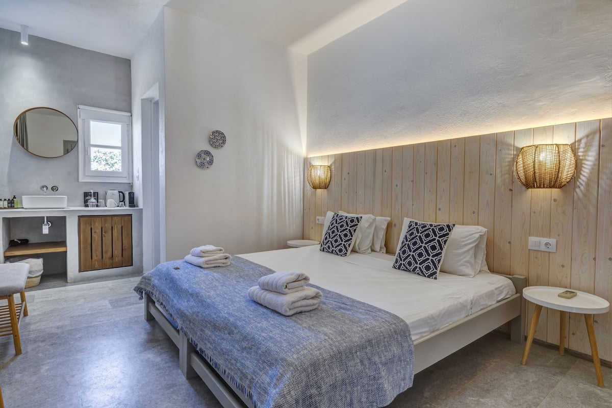 A bedroom with a bed, bedside table, and a bathroom with a sink and mirror.