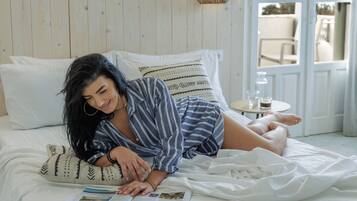 A bed with white bedding, a patterned pillow, and a small table with a glass of water and a bottle.