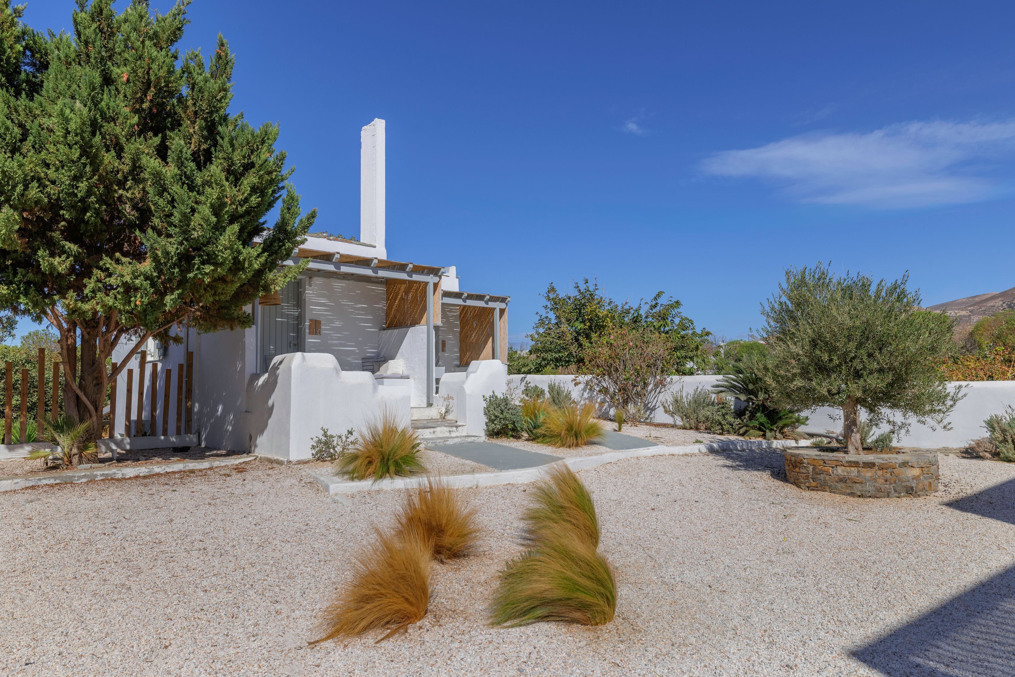 Un bâtiment moderne à la façade blanche, doté d’une haute cheminée blanche et d’une cour en gravier agrémentée de plantes ornementales.