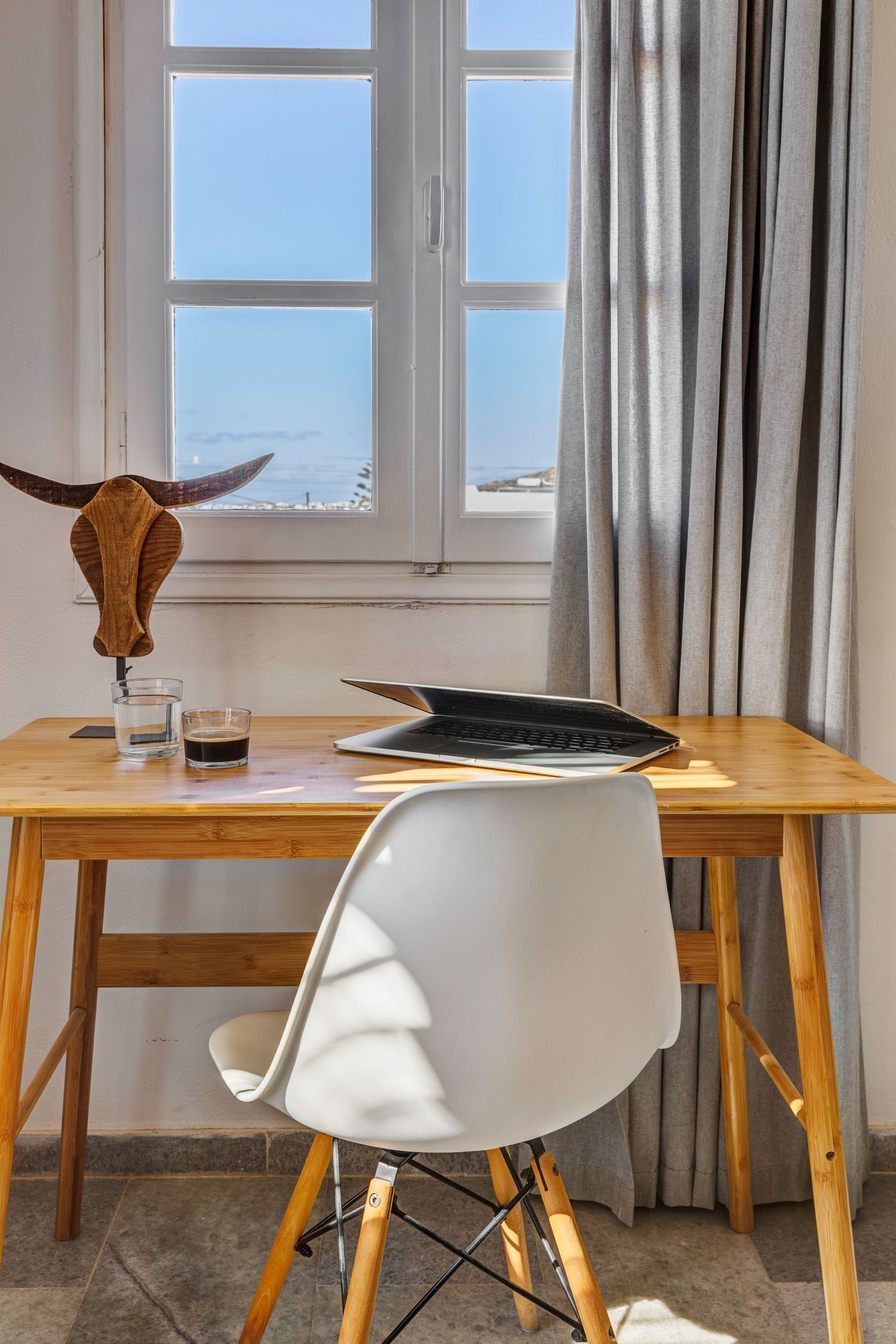 Una mesa de madera con una laptop, un vaso de agua y un objeto con forma de cuerno.