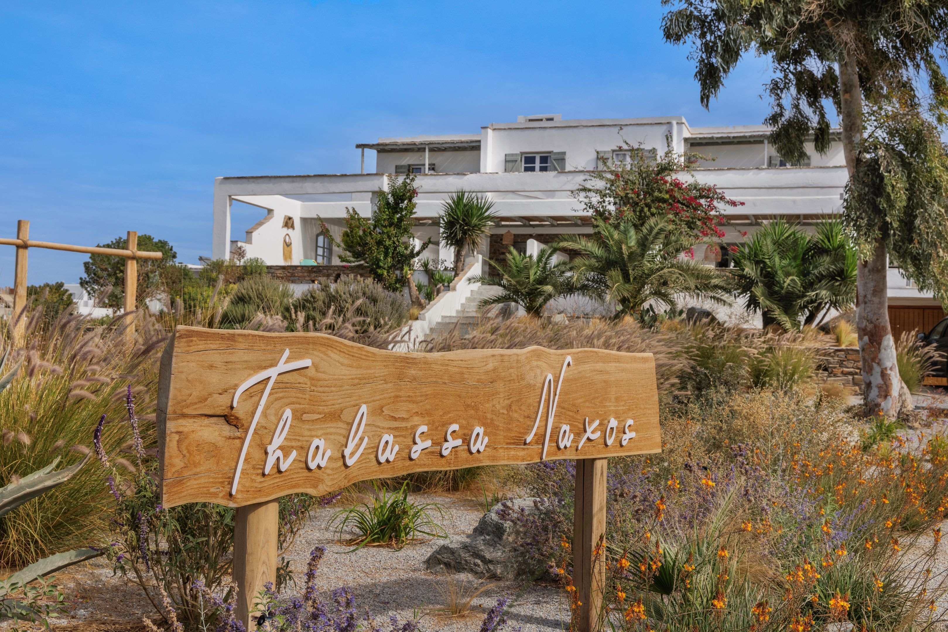 A wooden sign with the name 'Thalassa Naxos' in white cursive letters.