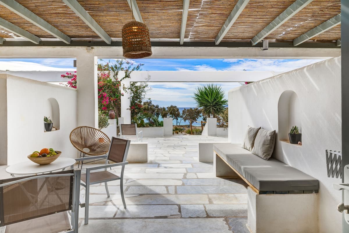 An outdoor patio with stone flooring, a white sofa, a wicker chair, a table with a fruit bowl, and a hanging light fixture.