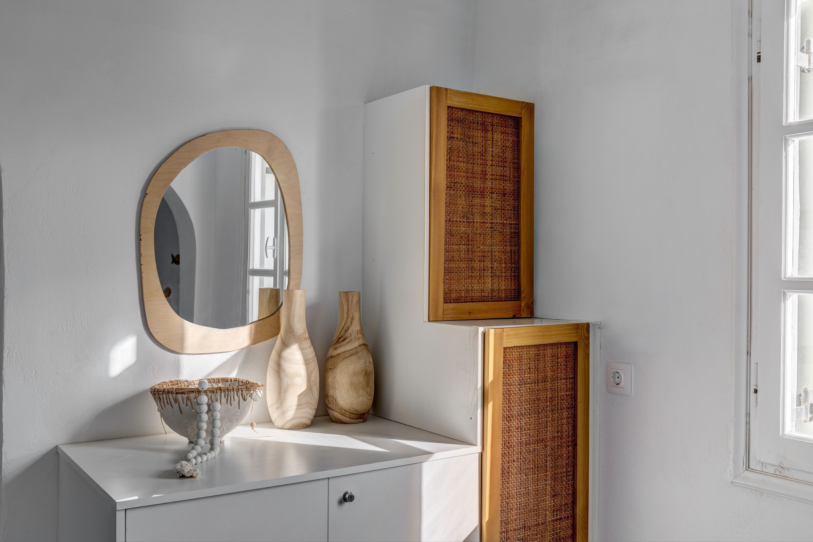 A white vanity with a round mirror, two vases, and a woven basket.