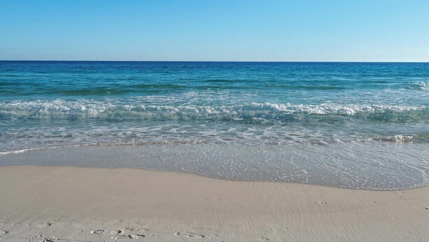 Une plage avec une eau d’un bleu limpide et un rivage sablonneux.