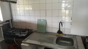 Cuina amb parets de rajola blanca, fogó de gas, rentapelats i taula de tall verd.