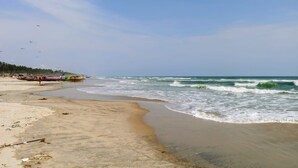 Una platja amb sorra, ones i embarcacions al fons.