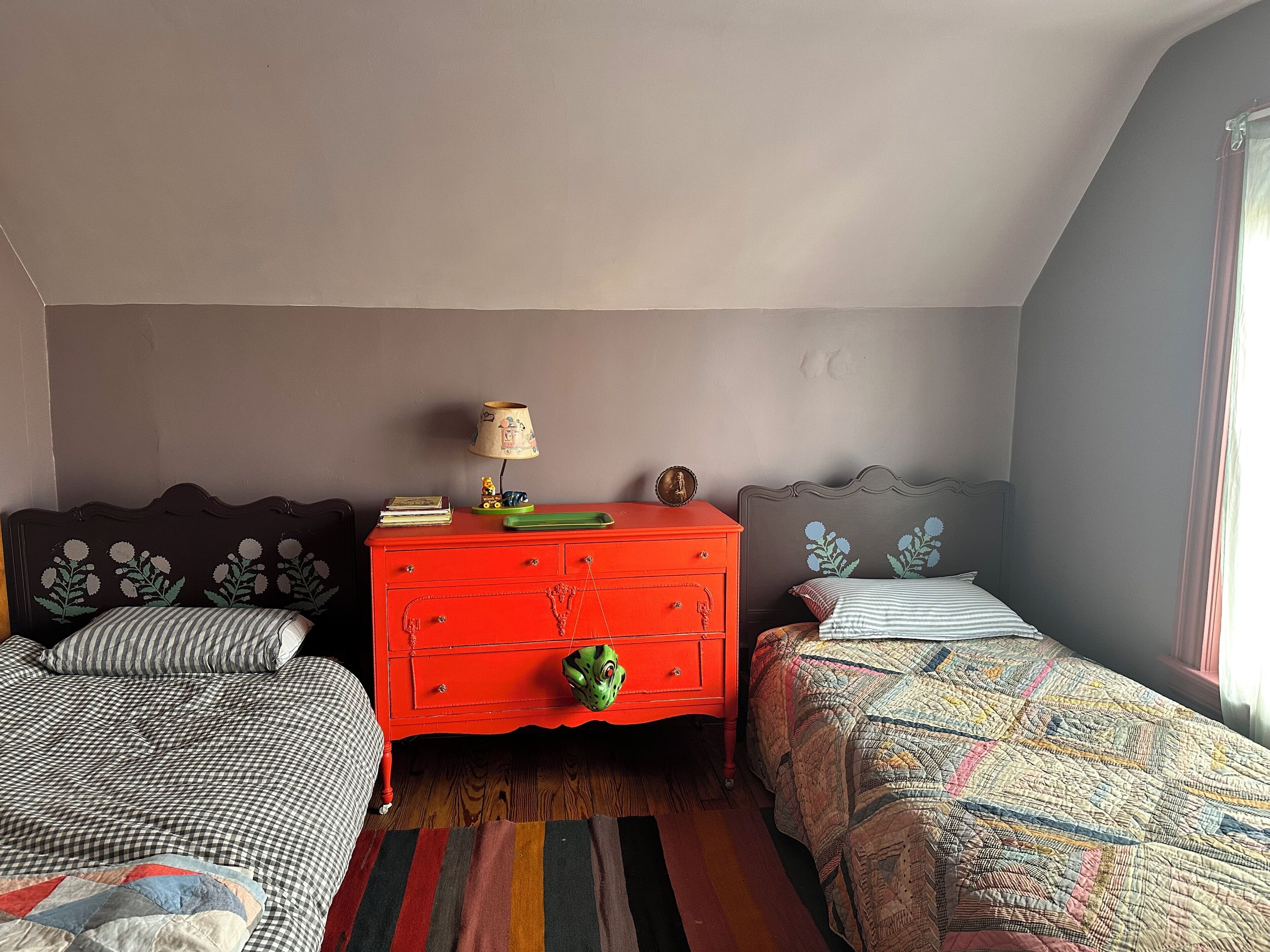 A bedroom with two beds, a red dresser, and a lamp.