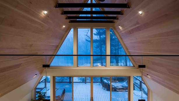 A high-ceilinged room with large windows and a view of a snowy deck.