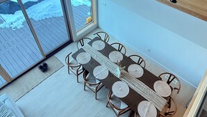 A modern interior with a wooden ceiling, a dining area with a long table and chairs, and a view of a snowy outdoor deck.