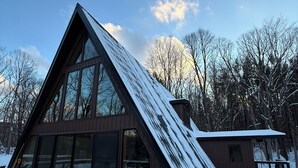 A modern, triangular-shaped house with large windows and a sloped roof covered in snow.