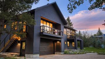 A modern two-story house with a balcony, large windows, and a stone pathway leading to the entrance.