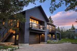 A modern two-story house with a balcony, large windows, and a stone pathway leading to the entrance.