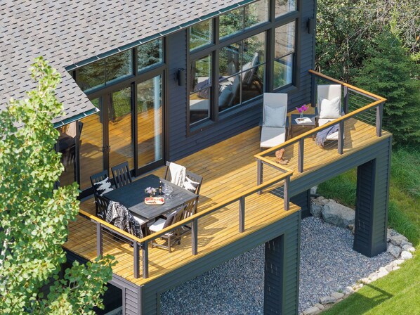 A modern deck with outdoor furniture, a dining table, and a view of the surrounding landscape.