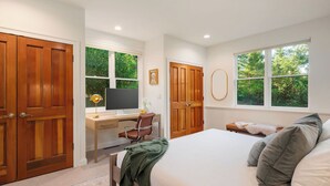 A bedroom with a bed, a desk, a chair, and two windows.
