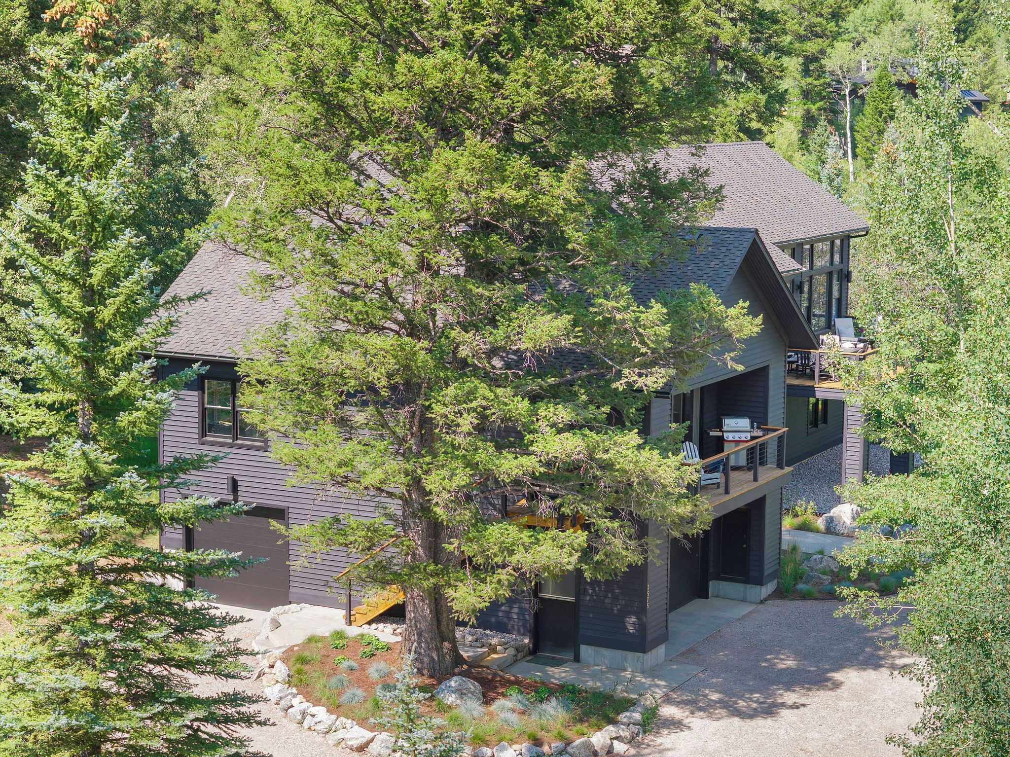 Une maison moderne à deux étages, dotée d’une terrasse et entourée d’arbres denses.