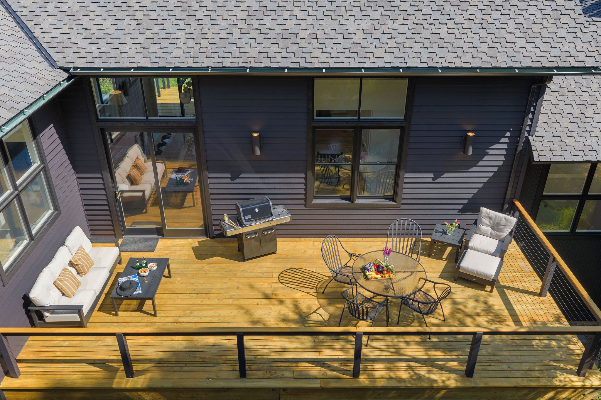 Une maison moderne dotée d’une terrasse, d’un espace salon extérieur et d’un coin barbecue.