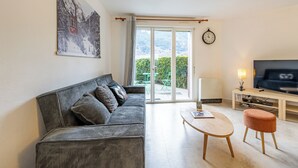 Ein Wohnzimmer mit einer Couch, einem Couchtisch, einem Fernseher und einer Schiebeglastür, die auf einen Balkon führt.