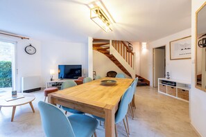 A modern living room with a wooden dining table, blue chairs, a TV, and a staircase.