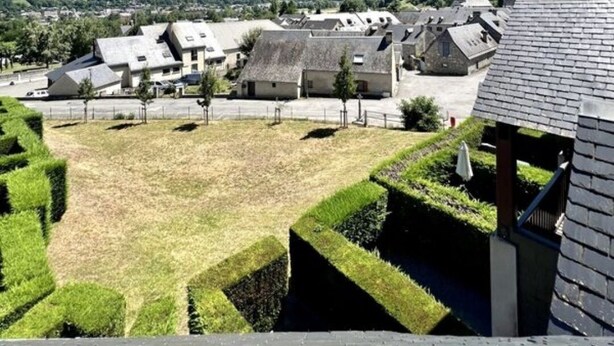 Blick auf ein Dorf mit traditioneller Bebauung, einer Rasenfläche und Bergen im Hintergrund.