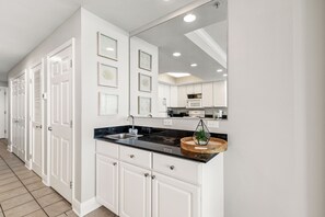 A modern kitchen with white cabinetry, a black countertop, and a wooden bowl on the sink. - San Carlos 1905 (Gulf Shores)
