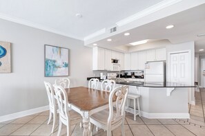 A modern kitchen with white cabinetry, a central island, and a dining area with a wooden table and white chairs. - San Carlos 1905 (Gulf Shores)