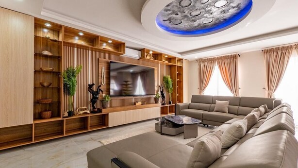A modern living room with a large sectional sofa, a flat-screen TV, wooden shelving with decorative items, and a ceiling with a circular design. - Very large 150 m² Studio with 320 degree sea view (Dakar)