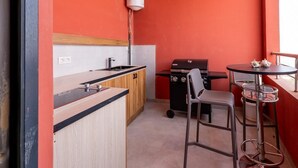 A compact kitchen with a wooden counter, a sink, and a black grill. There is a round table with two chairs and a small round table with a decorative item. - Very large 150 m² Studio with 320 degree sea view (Dakar)