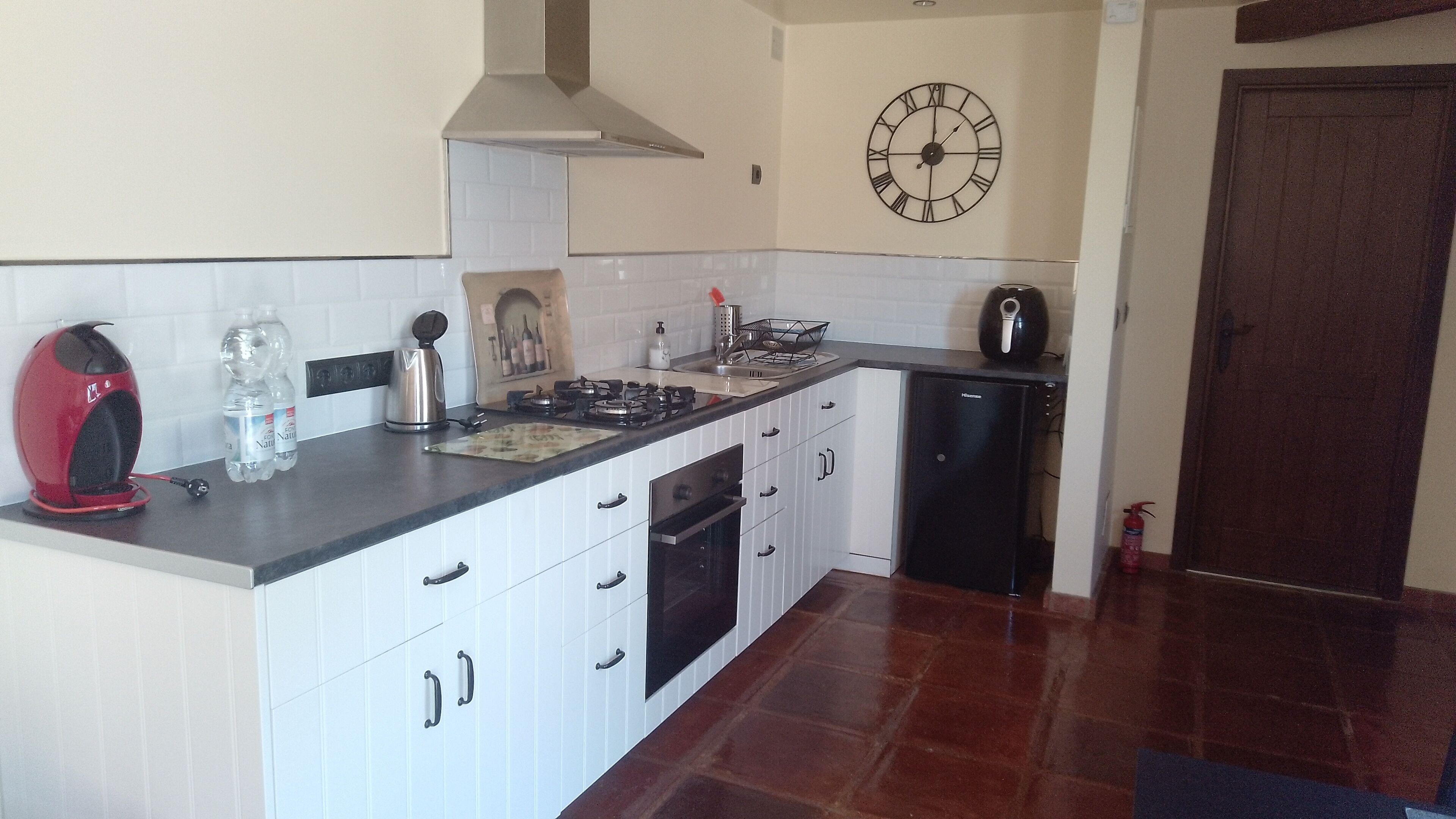 A compact kitchen with white cabinets, a black stove, and a clock on the wall.