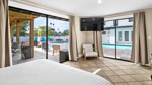 Ein Hotelzimmer mit einem großen Bett, einem Fernseher und einer Glastür, die zu einem Poolbereich führt.
