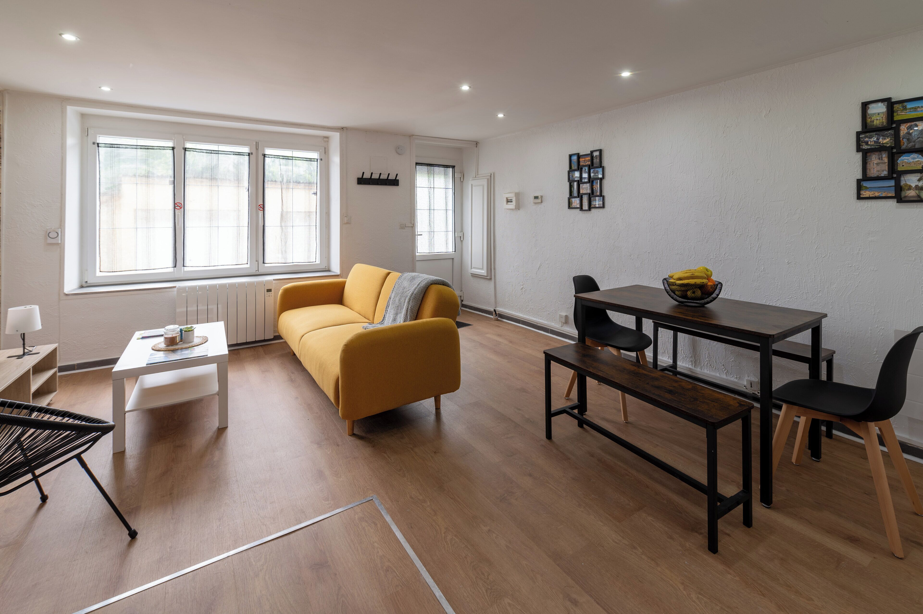 Ein modernes Wohnzimmer mit einem gelben Sofa, einem Esstisch mit Stühlen und großen Fenstern.
