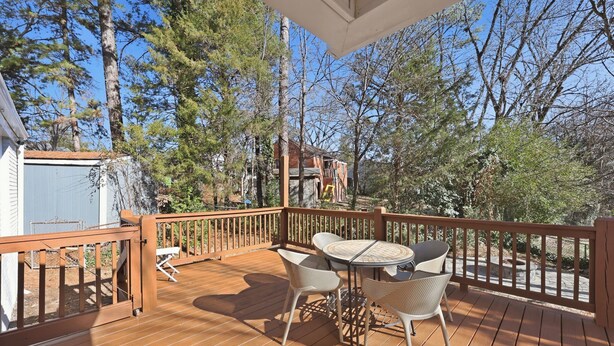 Une terrasse en bois avec une table et des chaises, entourée d’arbres et sous un ciel dégagé.