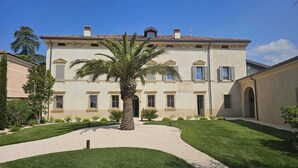 A large, two-story building with a symmetrical facade, multiple windows, and a central courtyard with a palm tree. - Relax and Comfort in an Elegant Venetian Villa with a Beautiful Outdoor Pool (Tregnago)